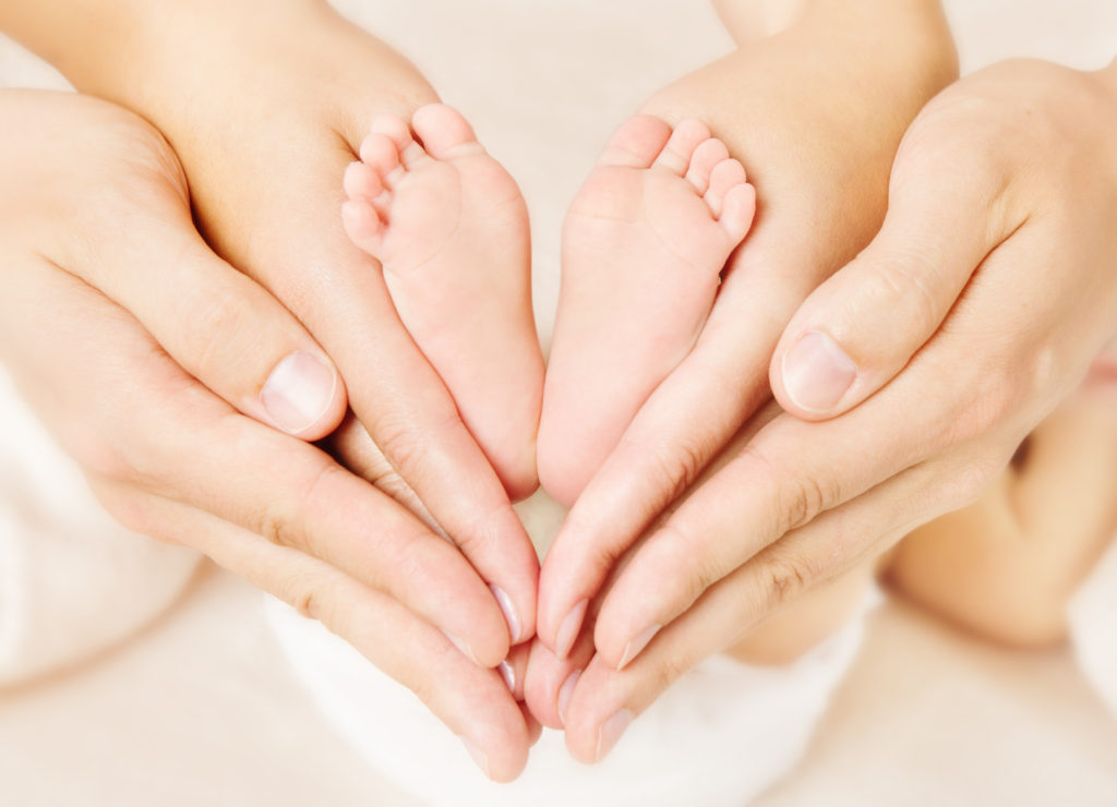 Newborn baby feet in parents hands. Love simbol as heart sign